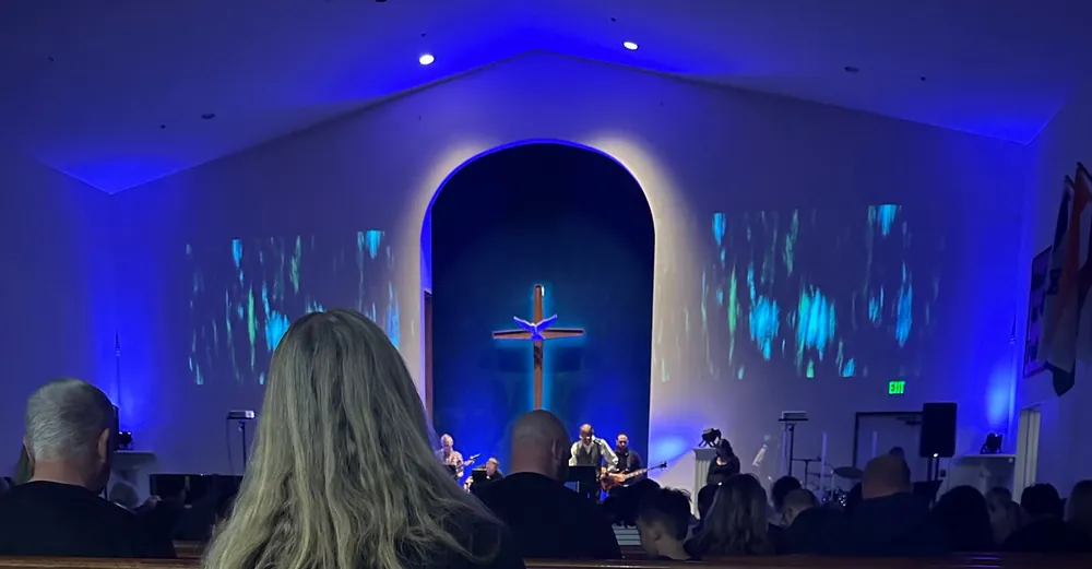 The congregation gathered for worship beneath a cross in the blue-lit sanctuary